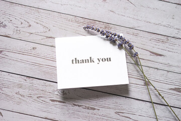 Thank you card on wooden table with a pair of lavender flowers. Elegant minimalist composition....