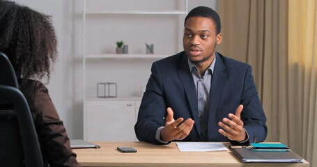 Afro American business man in formal suit being interviewed in modern IT marketing company sitting at meeting office showing his resume questionnaire to woman boss talking about professional skills