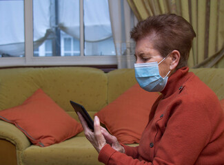 Senior woman wearing protective face mask talks with his family on video call during the coronavirus epidemic