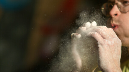 CLOSE UP: Cinematic shot of young male climber blowing excess chalk off fingers.
