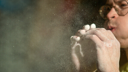 Obraz na płótnie Canvas CLOSE UP: Man climbing indoors blows into palms and removes magnesium powder.