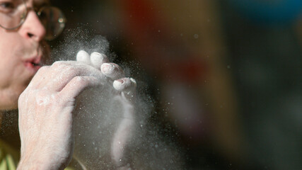Fototapeta na wymiar CLOSE UP: Man climbing indoors blows into his hands and removes magnesium powder