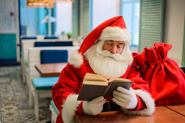 Santa Claus is sitting in a cafe and reading a book