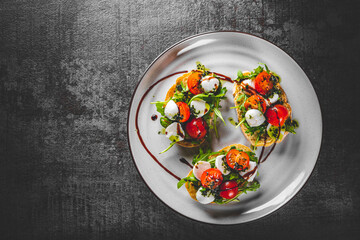 Italian bruschetta with roasted tomatoes, mozzarella cheese, balsamic vinegar and herbs on plate