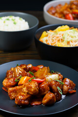 Sweet and sour chicken, fried rice with egg and glass noodles salad served in ceramic bowls. Dark wooden table, high resolution