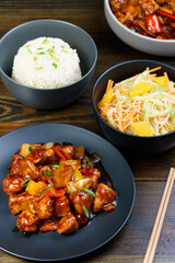 Sweet and sour chicken, fried rice with egg and glass noodles salad served in ceramic bowls. Dark wooden table, high resolution