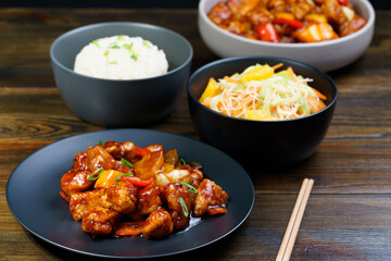 Sweet and sour chicken, fried rice with egg and glass noodles salad served in ceramic bowls. Dark wooden table, high resolution