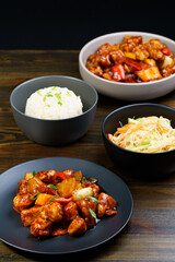 Sweet and sour chicken, fried rice with egg and glass noodles salad served in ceramic bowls. Dark wooden table, high resolution