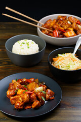 Sweet and sour chicken, fried rice with egg and glass noodles salad served in ceramic bowls. Dark wooden table, high resolution