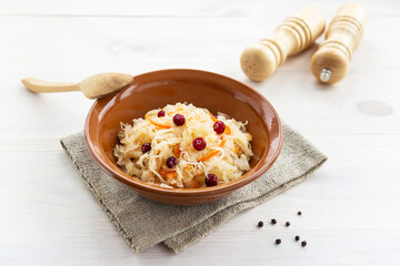 Sauerkraut with cranberries in a clay bowl with a wooden spoon. Russian traditional food.