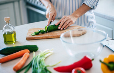 Close up photo of young smiling woman is preparing a fresh healthy vegan salad with many vegetables in the kitchen at home and trying a new recipe