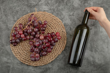 Naklejka premium Cluster of red grapes and woman hand holding bottle of wine on marble surface