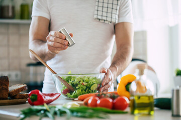 Close up photo of young male hands is preparing wonderful fresh vegan salad in the kitchen at home