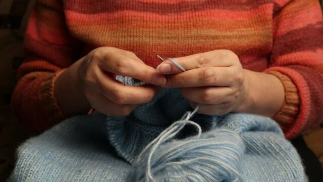 hands knitting a sweater of blue wool yarn with knitting needles