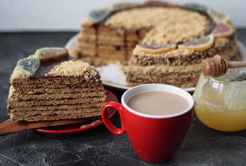 Homemade honey puff cake with a piece of sliced on a red plate with a cup of coffee and honey on a dark background.Food background in rustic style.