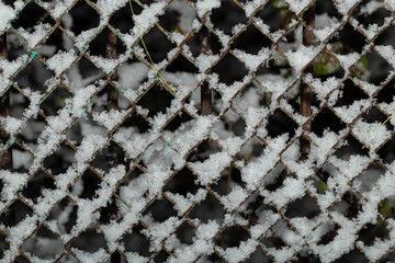 Snow piled on the wires of a chain link fence, on a winter night.