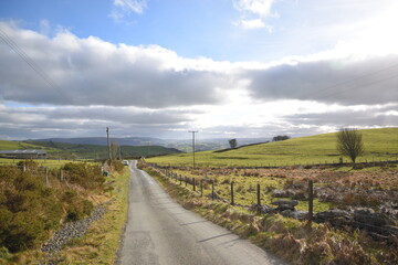 Fototapeta na wymiar a small road that leads to llyn marw near caersws in wales, surrounded by fields and barbed fences