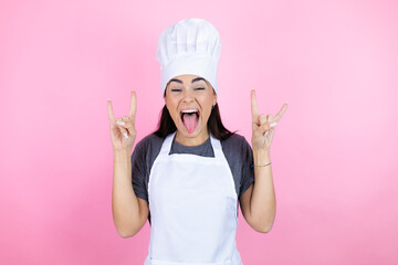 Young hispanic woman wearing baker uniform over pink background shouting with crazy expression...