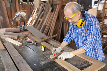senior asian man carpenter wearing glasses and headphone, measuring wood with ruler in workshop