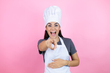 Young hispanic woman wearing baker uniform over pink background laughing at you, pointing finger to the camera with hand over body, shame expression