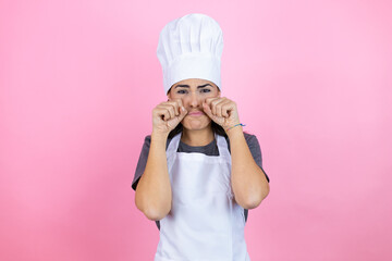 Young hispanic woman wearing baker uniform over pink background depressed and worry for distress, crying angry and afraid. Sad expression.