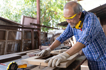 senior asian man carpenter using sandpaper on a piece of wood in workshop