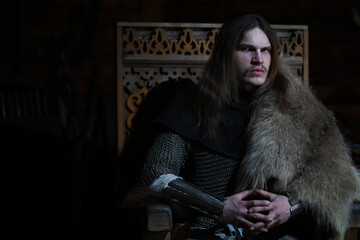 A mighty hero with long hair in chain mail armor in an ancient hall. Medieval warrior in the knight's chambers.