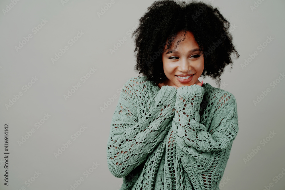 Wall mural Posing in a photo studio smiling. copy space. Portrait of a Happy Beautiful Young Afro Appearance. The woman is dressed in a modern warm mint-colored sweater.