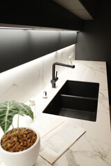 Modern kitchen with black furniture, White marble worktop and backsplash. Black sink and tap, Light under wall cabinet.