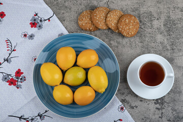 Cup of hot tea, plate of lemons and delicious biscuits on stone surface