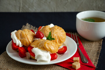mouthwatering eclairs with ice cream, whipped cream and fresh strawberries with a cup of green tea, the perfect dessert
