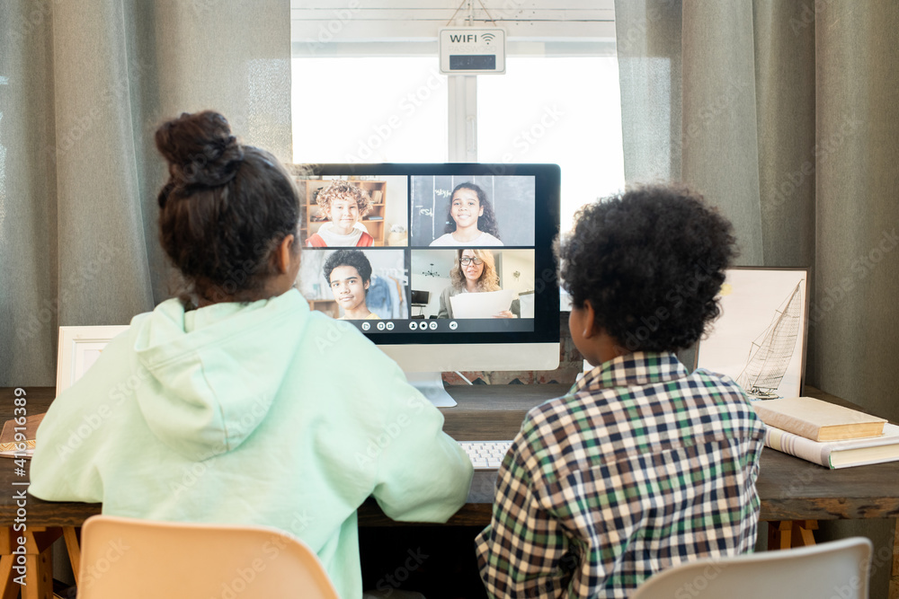 Poster rear view of diligent schoolchildren in casualwear sitting in front of computer
