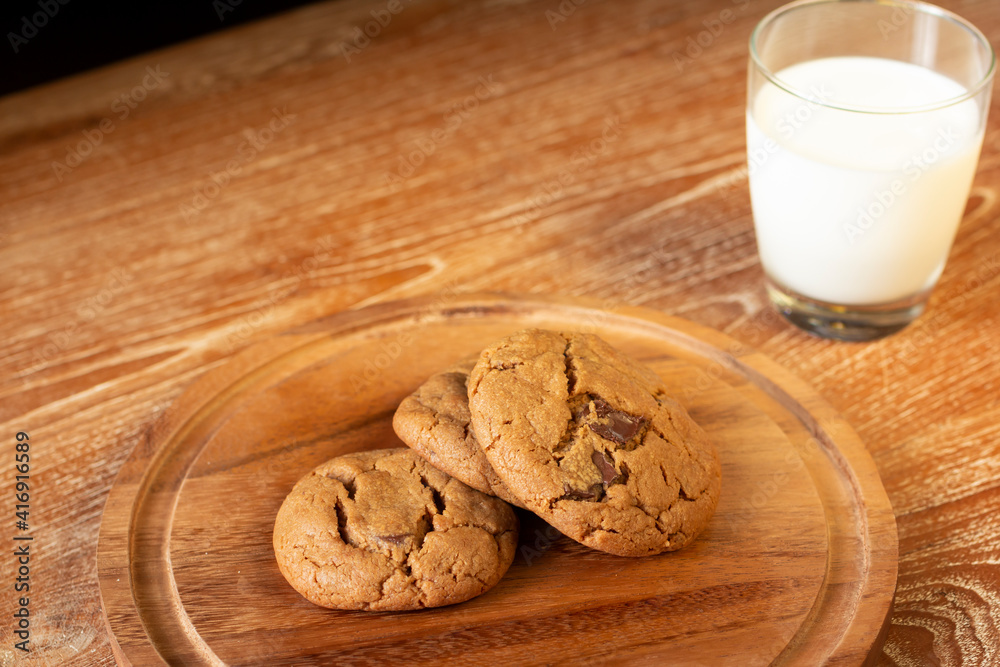 Wall mural Delicious Chocolate Chip Cookies on wooden plate on wooden table. Fresh baked chocolate chip cookies on rustic wooden table. Homemade Chocolate Chip with milk glass on the background.