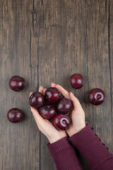 Woman hands holding healthy purple plums on wooden table