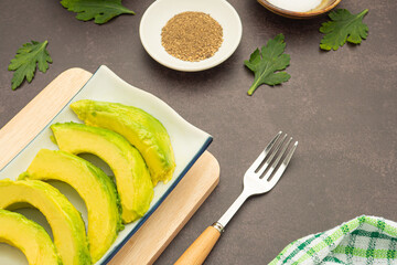 The sliced avocados are placed on a white plate with cutlery and cloth placed on a dark gray background. Space for text. Close-up photo. Concept of healthy fruits
