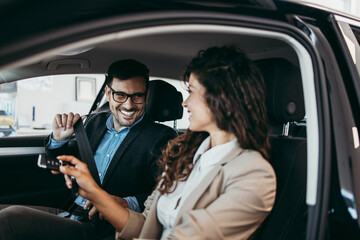 Happy middle age couple enjoying while choosing and buying new car at showroom.