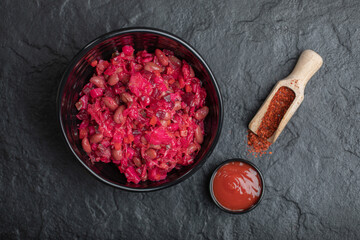 Bowl of pickled cabbage with beans and ketchup on black background