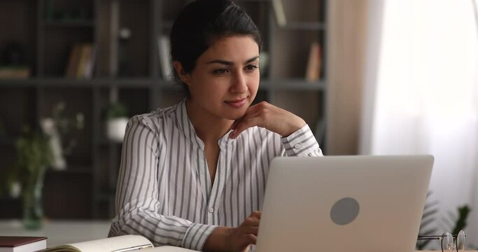 Concentrated young indian ethnic female freelancer entrepreneur looking at computer screen, working on difficult task at home office. Focused millennial multiracial woman studying distantly online.