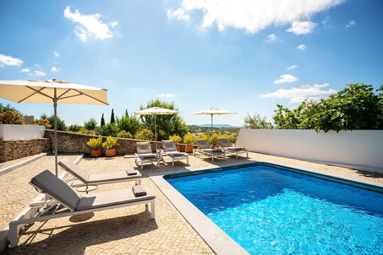 Loungers placed on the left and in the front of a pool with clean looking water on a sunny day.