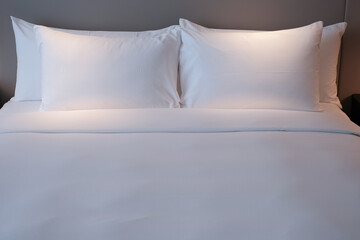 Clean Bedding sheets and pillow on natural wall room background. White bedding and pillow in hotel room. White pillows on empty bed. - obrazy, fototapety, plakaty