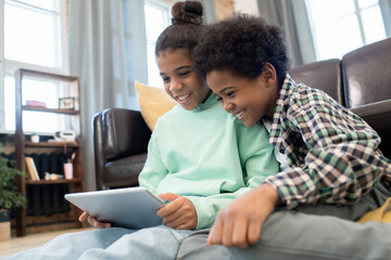 Happy affectionate siblings watching video on the floor by couch in living-room