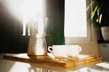 Geyser coffee maker made of aluminum metal. two white mugs for coffee Americano espresso. It's on the table. Hot, aromatic Americano coffee. Sunlight from the window.