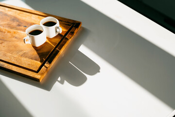 Two ceramic cups of white light coffee. A hot, flavorful drink. Americano and espresso are two servings on the table . Morning light from the window. An invigorating drink instead of an energy drink.