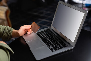 Cropped photo of hands of man using laptop at home, holding credit card, online home shopping, banking business.