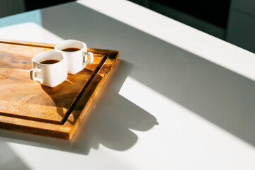 A hot, flavorful drink. Two ceramic cups of white light coffee. Americano and espresso are two servings on the table . Morning light from the window. An invigorating drink instead of an energy drink.