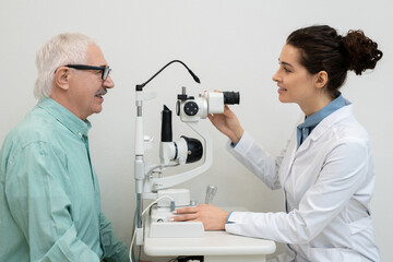 Ophthalmologist using medical equipment while testing eyesight of male patient