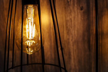 Modern retro style lamp in a shade made of metal rods against a background of a wooden wall. Copy space
