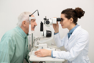 Naklejka na ściany i meble Young brunette female ophthalmologist working with senior patient in clinics