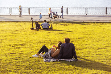 A young girl and an adult man are resting on the embankment against the background of walking people. View from the back. Unrecognizable people