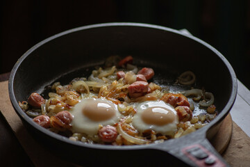 Chicken egg fried in a pan with onions and sausages, close-up.